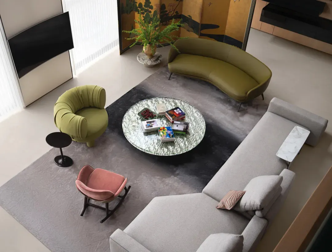 Modern living room with textured furniture, round glass coffee table, and curved sofas, featuring a vase of flowers and books