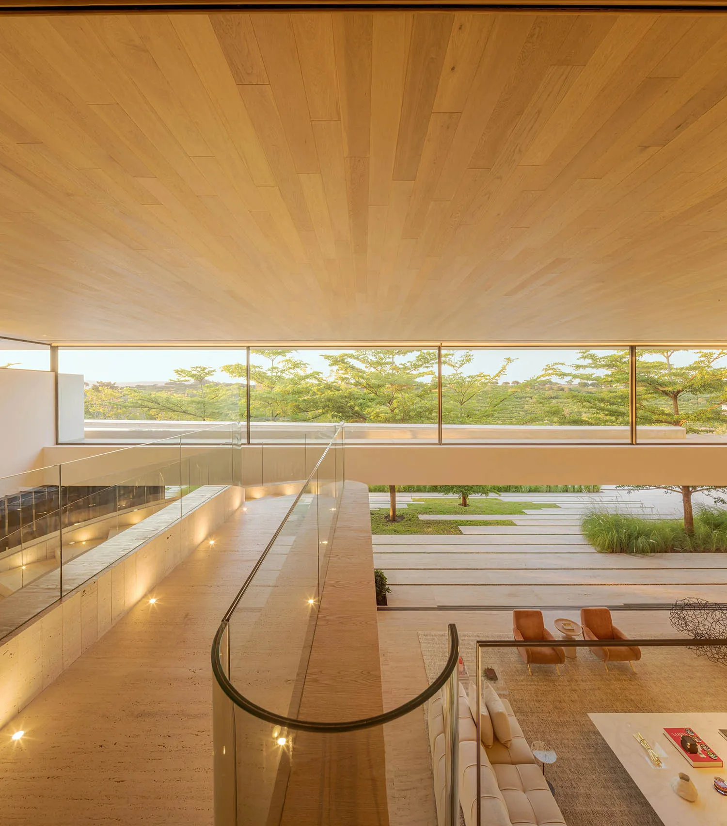 A modern living room with wooden floors, glass walls, and large windows overlooking greenery.