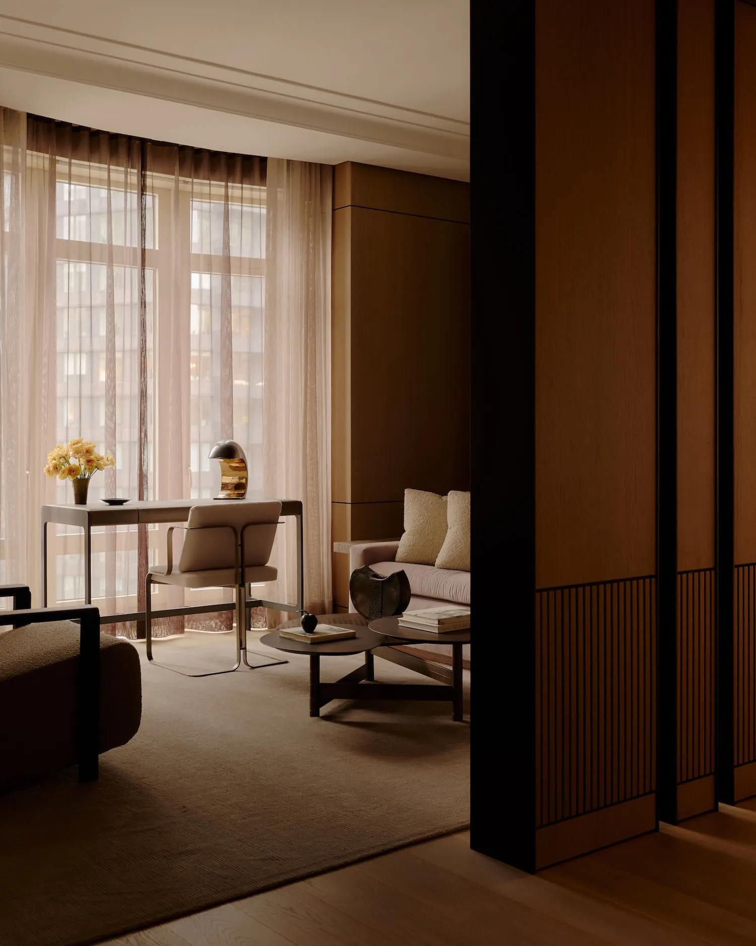 A modern minimalist living room featuring brown wood elements, a leather sofa, and a plush fabric armchair.