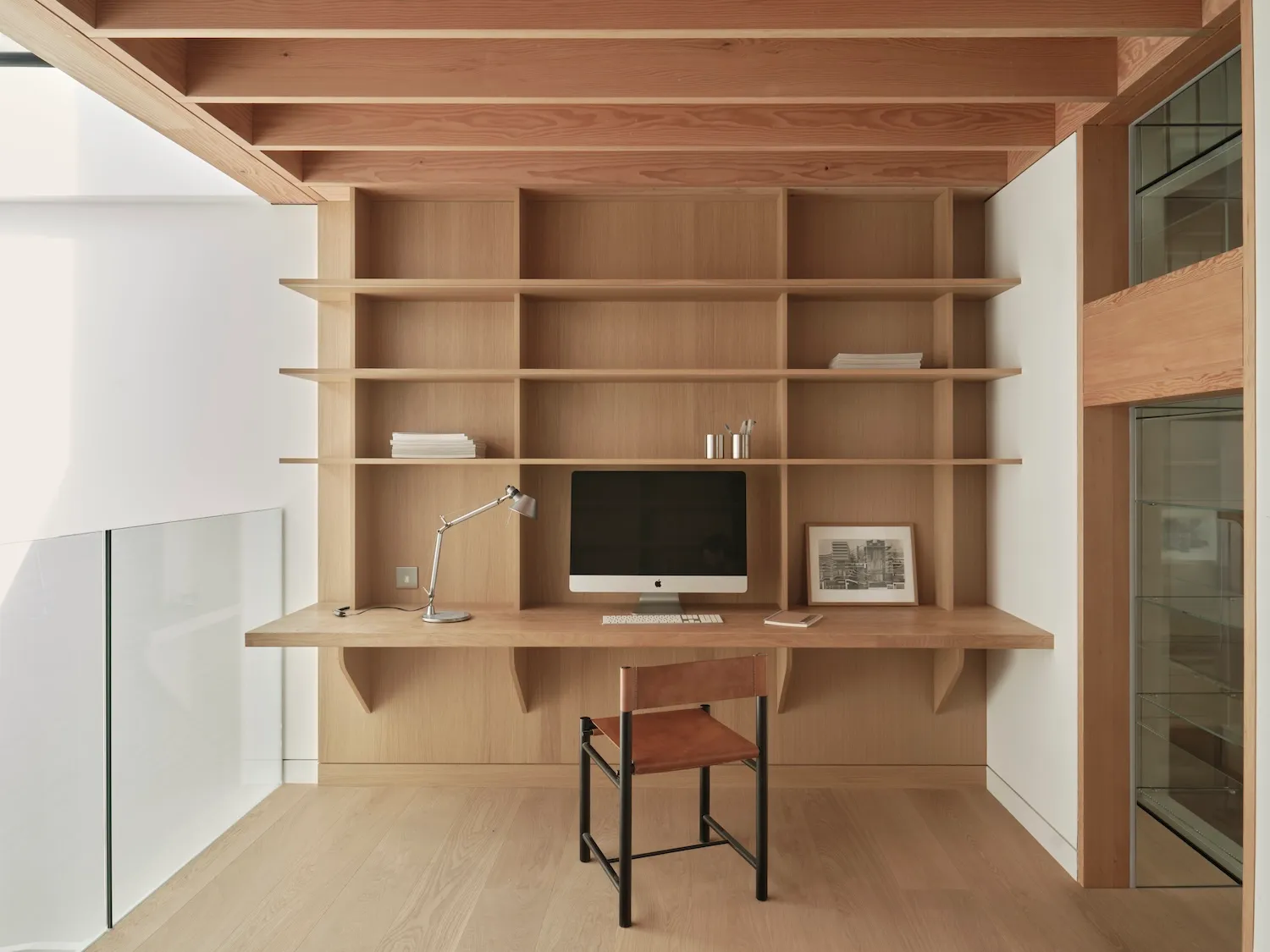 A minimalist study with wooden desk, shelves, and chair.