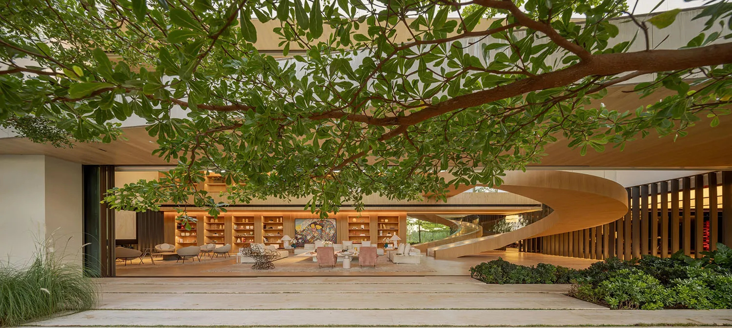 Modern residential living room featuring wood flooring and furniture, with a spiral staircase and greenery.