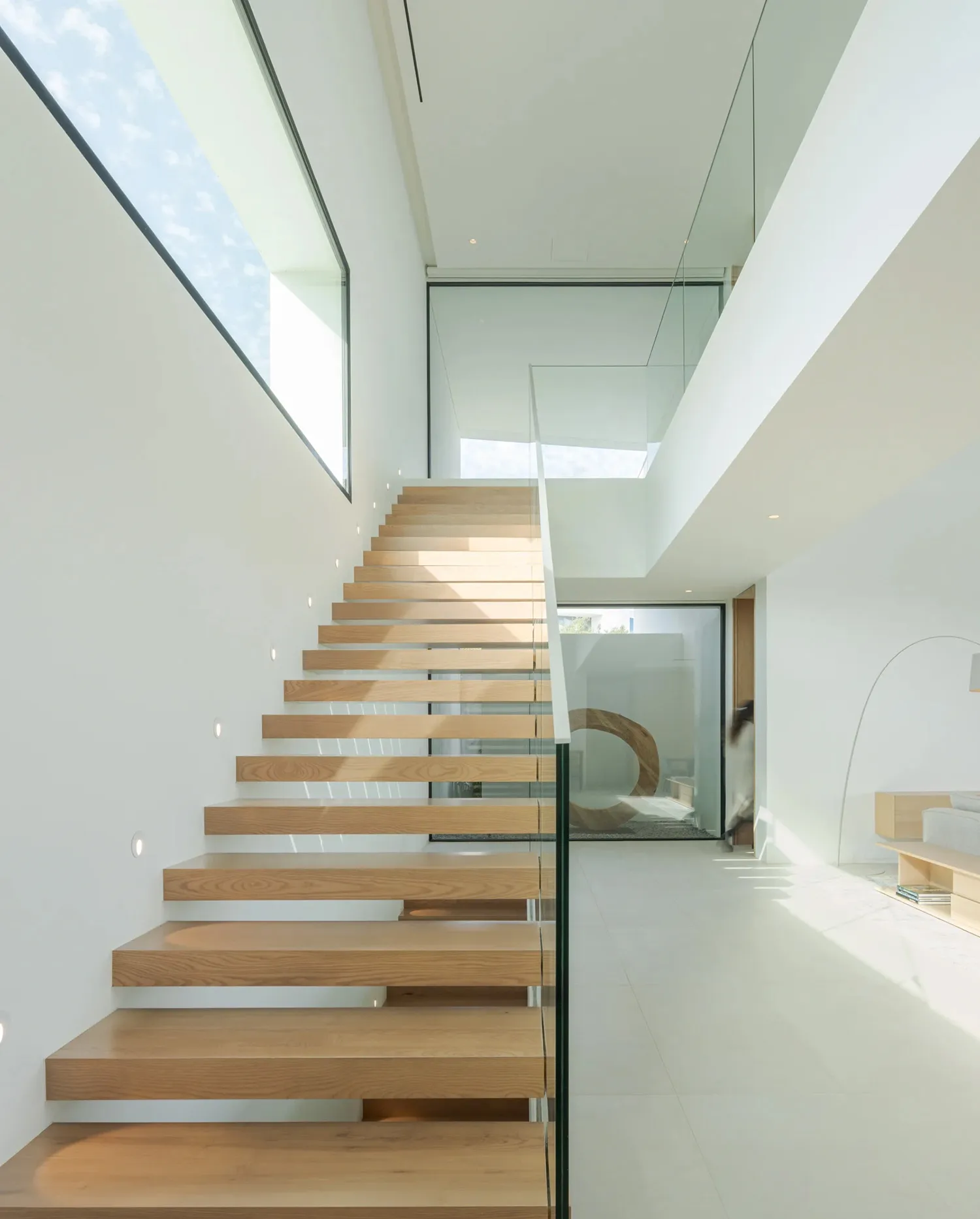 Modern staircase featuring wood steps, glass balustrade, and concrete floor.