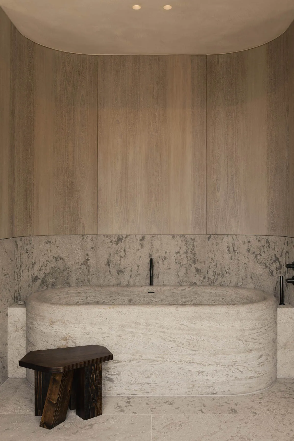 A minimalist bathroom featuring a marble bathtub and wooden accents.