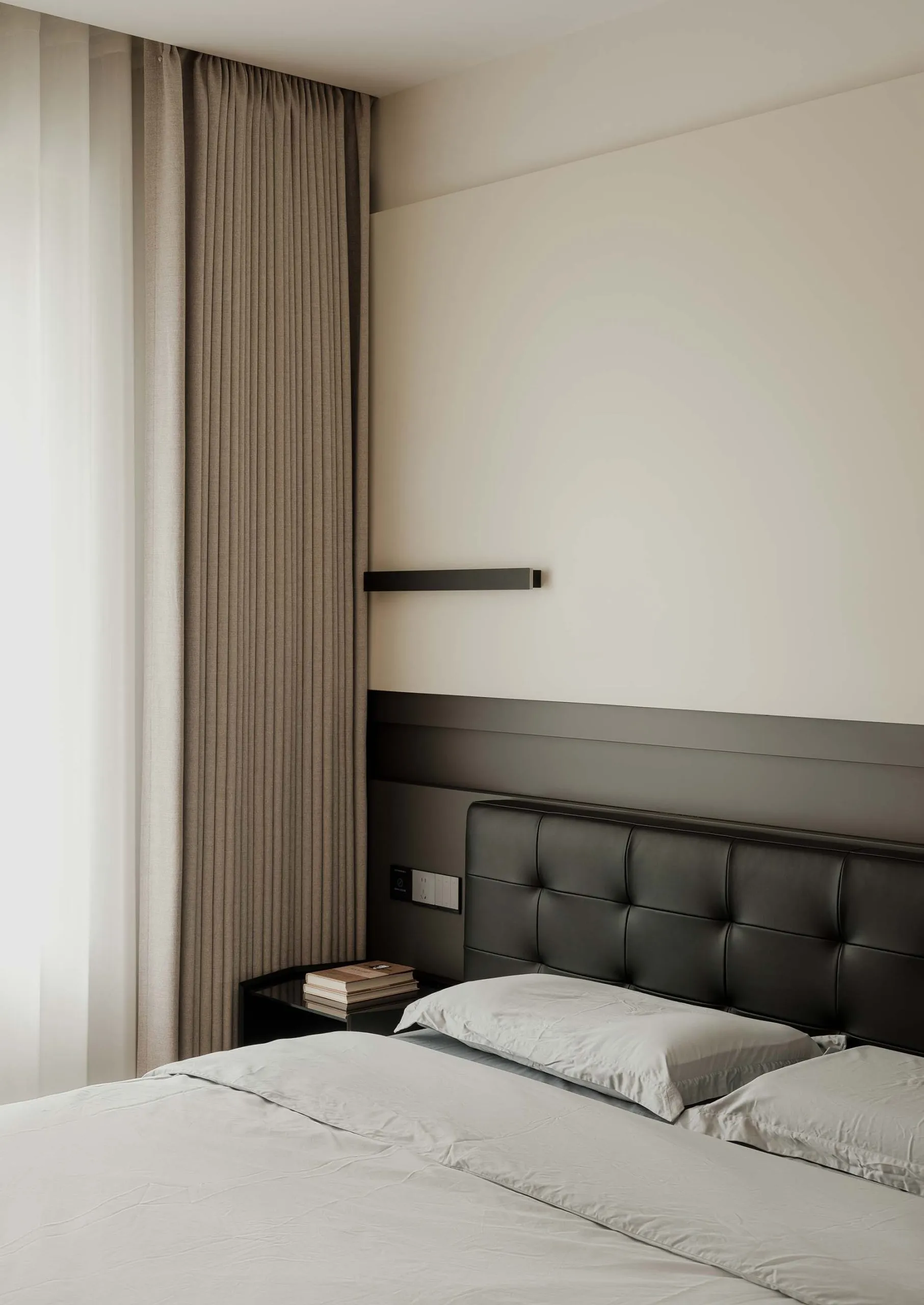 A minimalist bedroom featuring fabric curtains and a leather headboard with a side table and books.