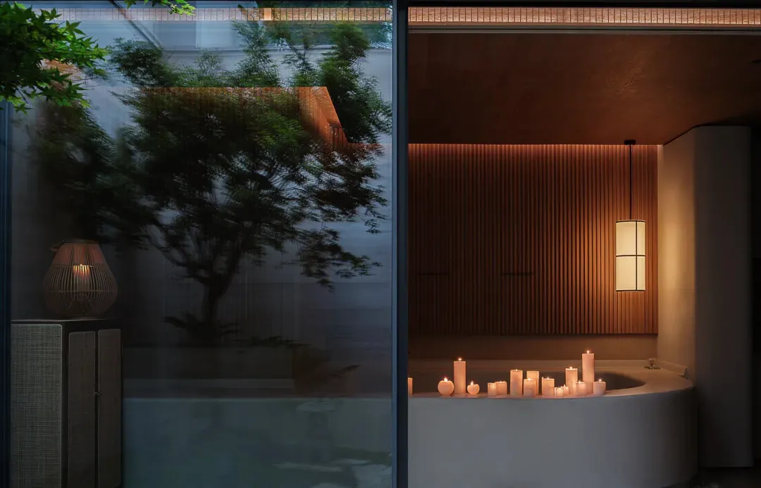 A serene minimalist hotel bathroom with wooden walls and a bathtub adorned with lit candles.
