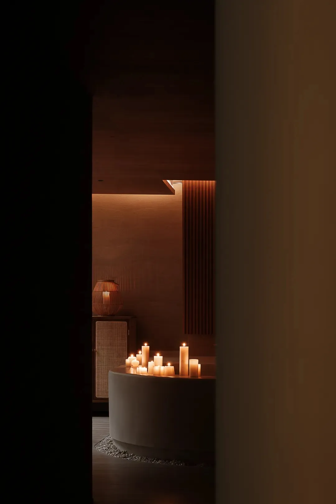 A modern bathroom featuring a concrete bathtub surrounded by candles and a wooden shelf.