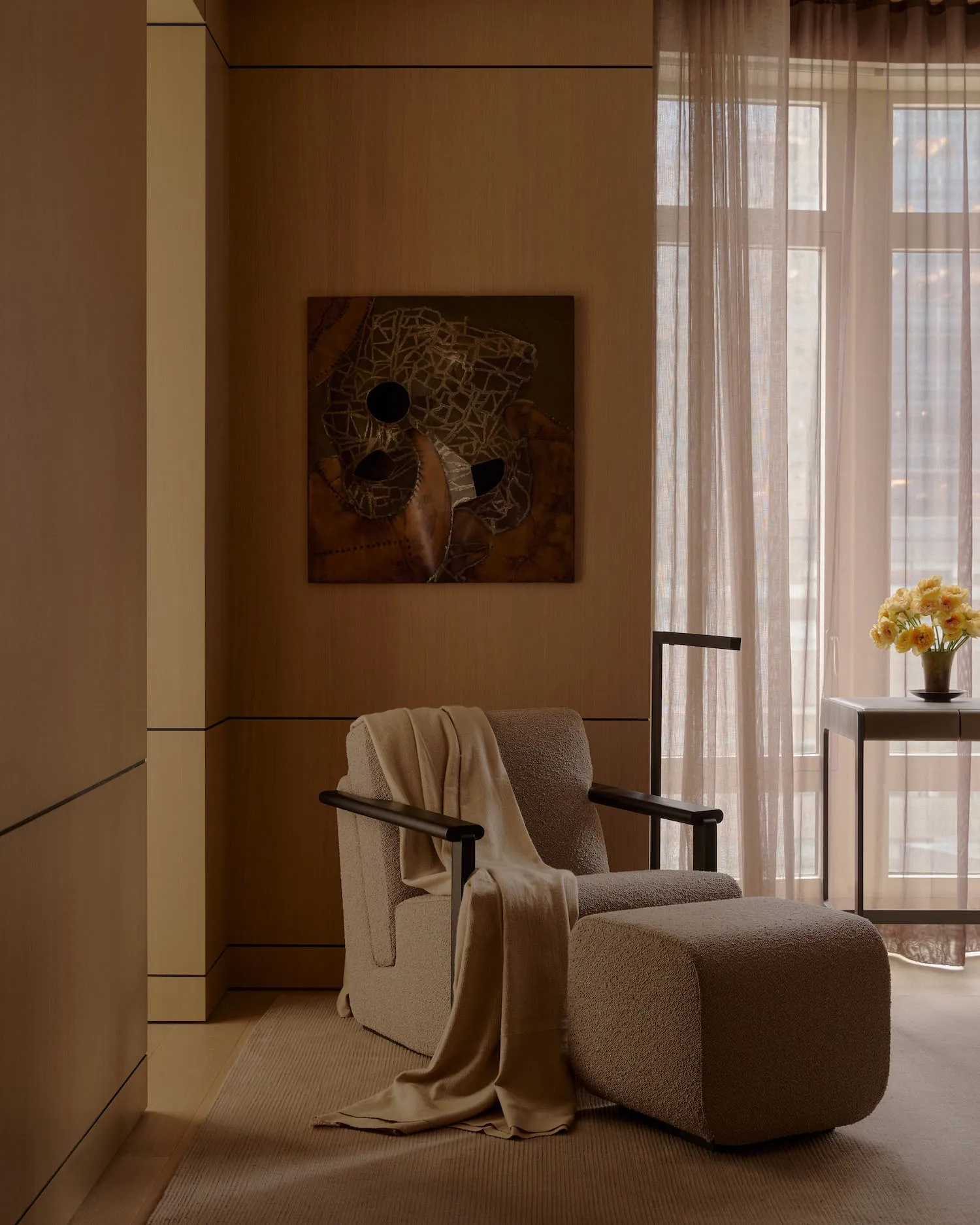 A cozy modern living room with a beige armchair, matching ottoman, and fabric drapes.