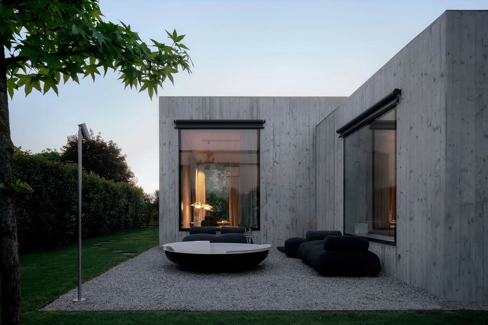 A modern minimalist exterior with concrete walls, large windows, and outdoor seating area.