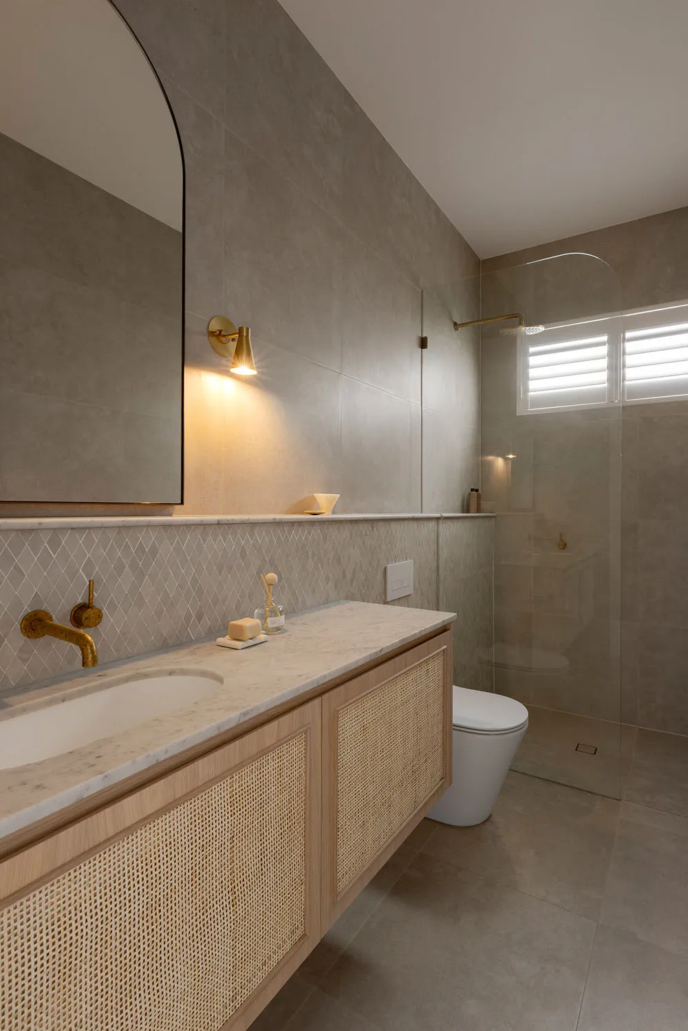 Modern minimalist bathroom with concrete tiles, floating vanity with rattan accents, and gold fixtures.