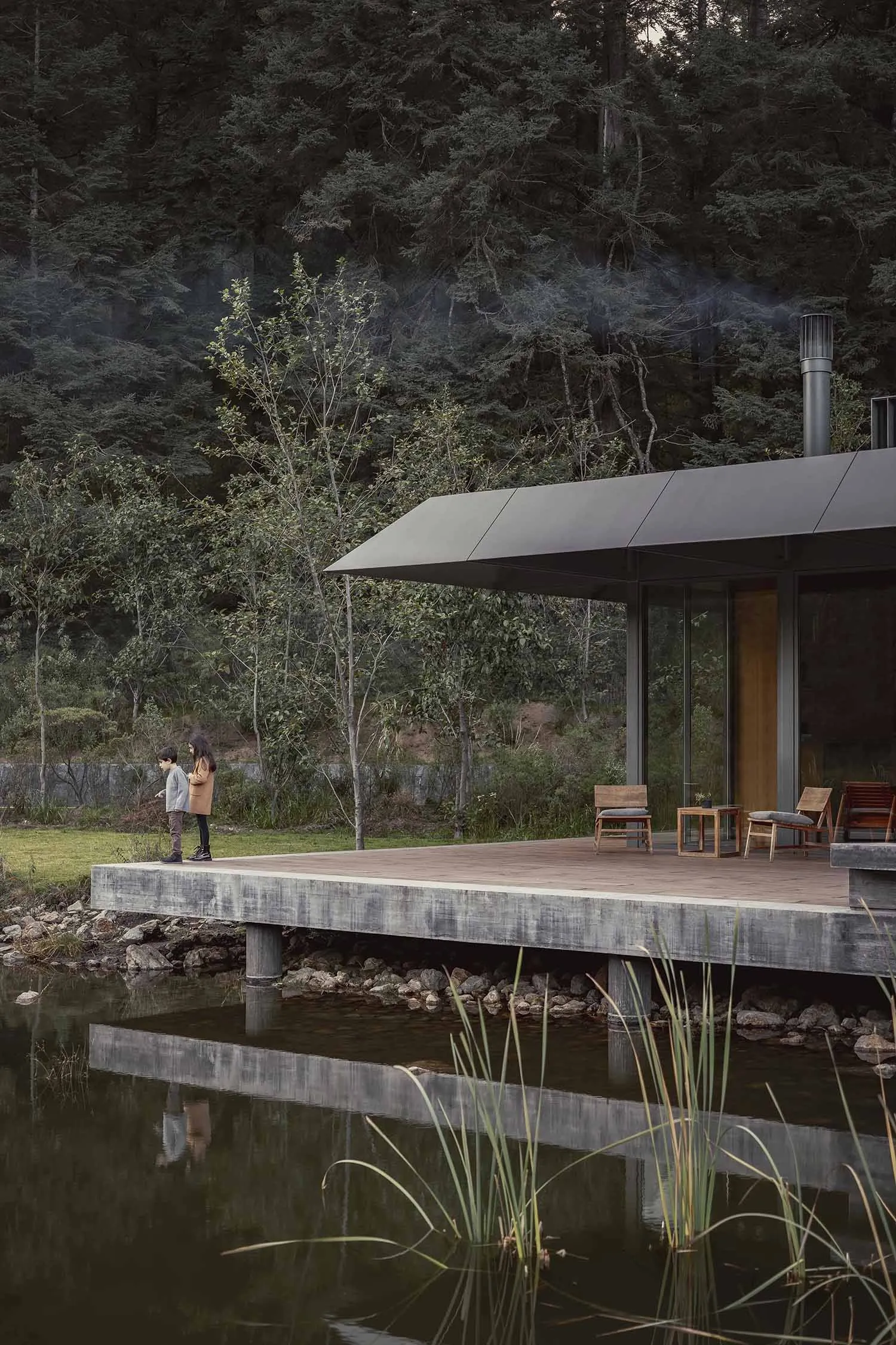 A minimalist house with a pool and cabin, featuring a concrete deck and wooden furniture.