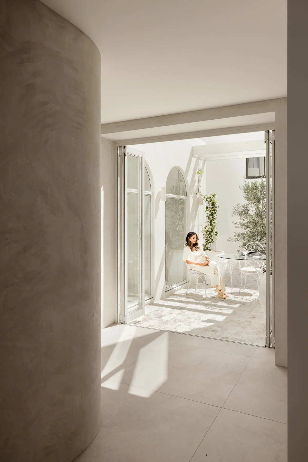 A modern interior with light concrete walls and a woman sitting on a chair in a bright, spacious room.