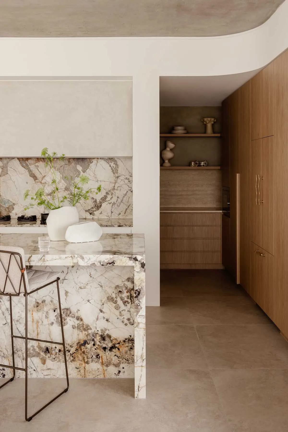 Marble kitchen counter with a white vase containing green plants and a glass of water on it.