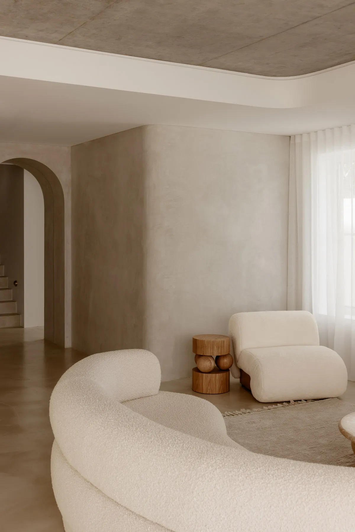 A modern minimalist living room with white velvet sofas, concrete walls, and wooden side tables.