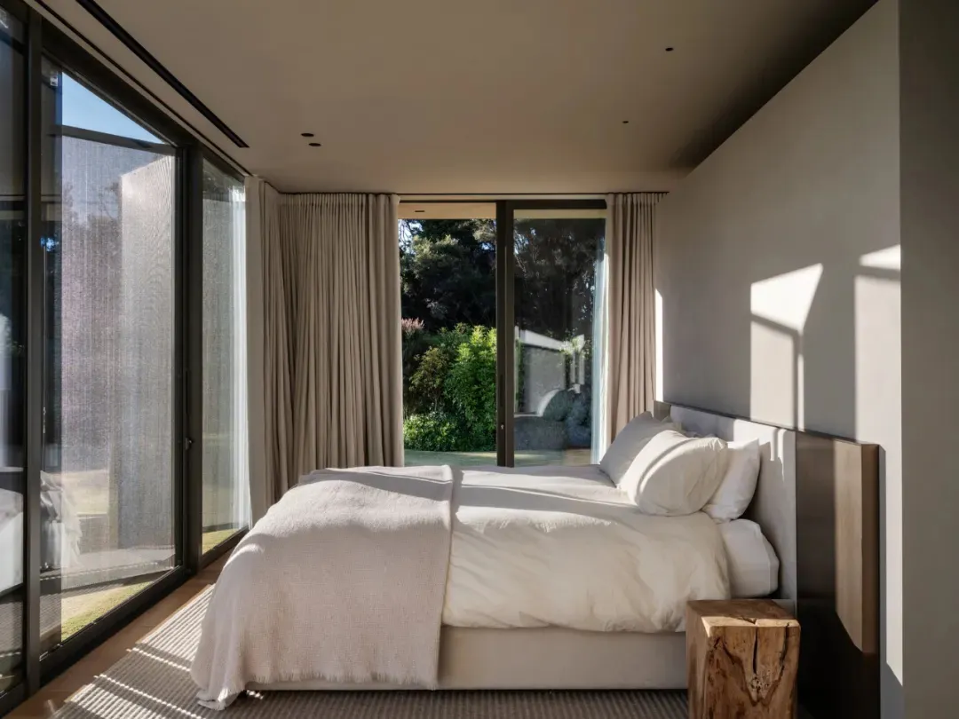 A minimalist bedroom featuring a glass door and white bedding.