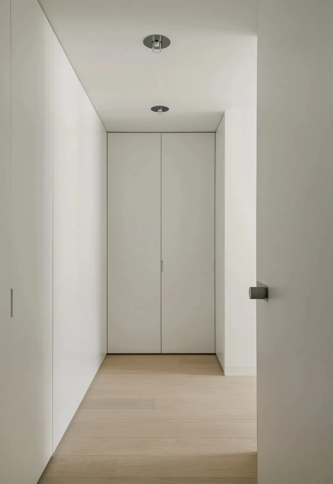 A minimalist interior with white paneled walls and a light wood floor.
