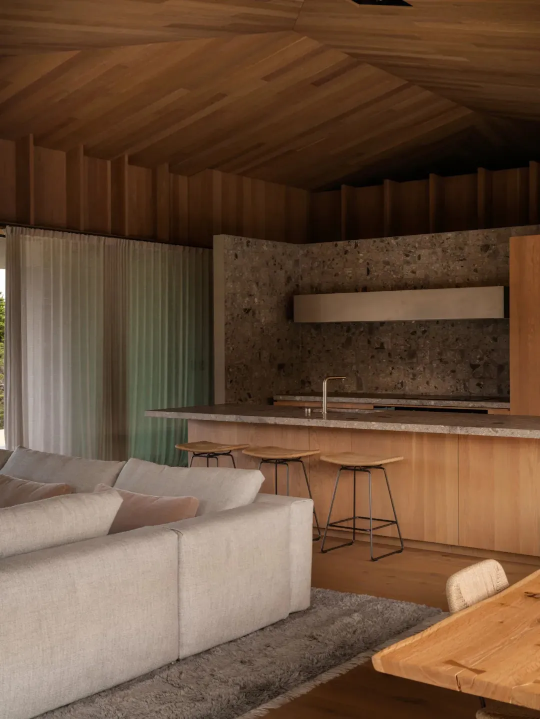 Modern minimalist kitchen featuring a wood countertop, wooden stools, and a stone backsplash.