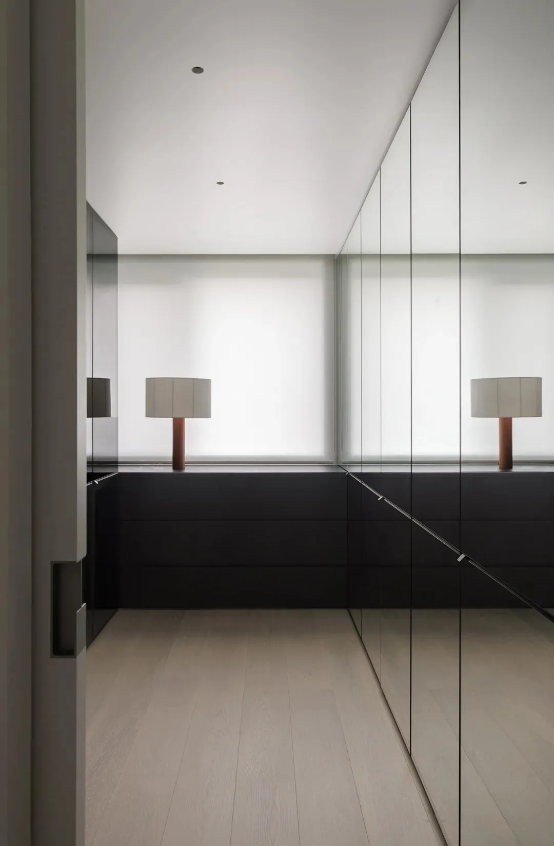 Modern minimalist wardrobe with glass doors and a single table lamp with a white shade and wooden base.