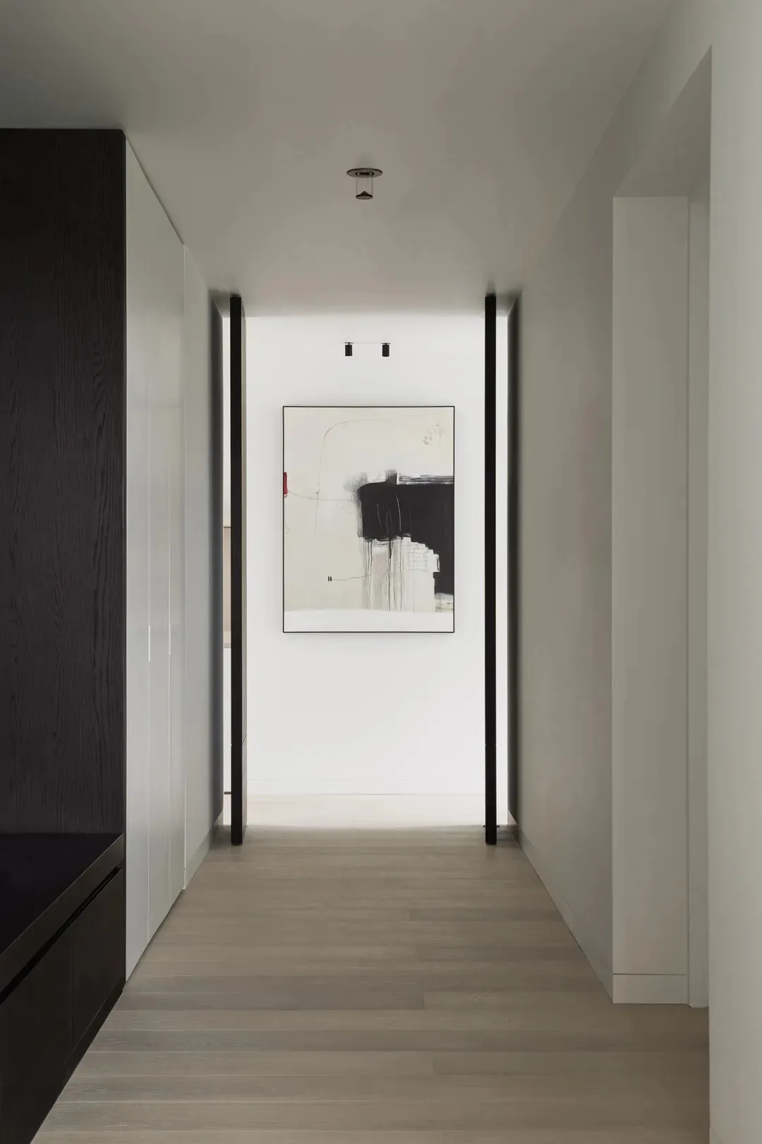 A modern hallway with minimalist black and white decor, featuring abstract art on the wall and dark wooden cabinets.