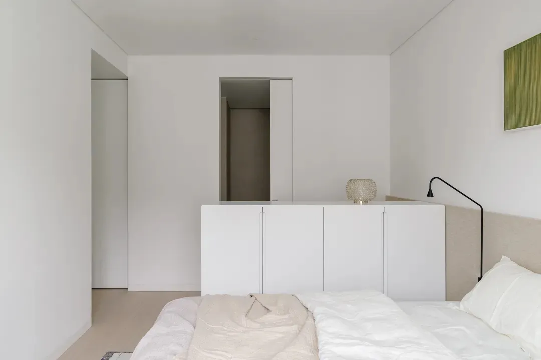 Modern minimalist bedroom with white bed set and wooden floor.