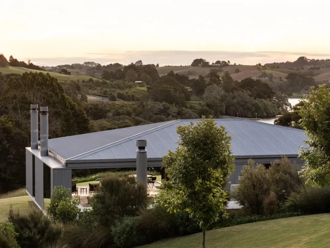 A modern rural house with a metal-clad roof surrounded by greenery and hills.