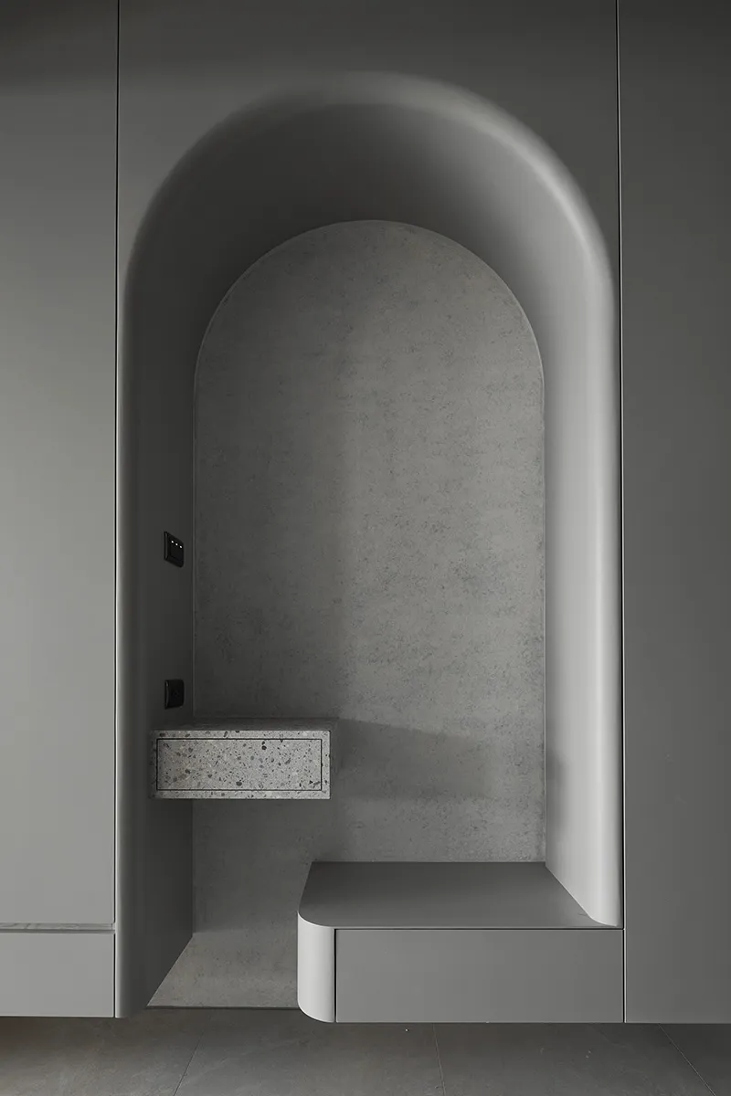 A modern interior design featuring a concrete niche with a floating shelf and seating area.