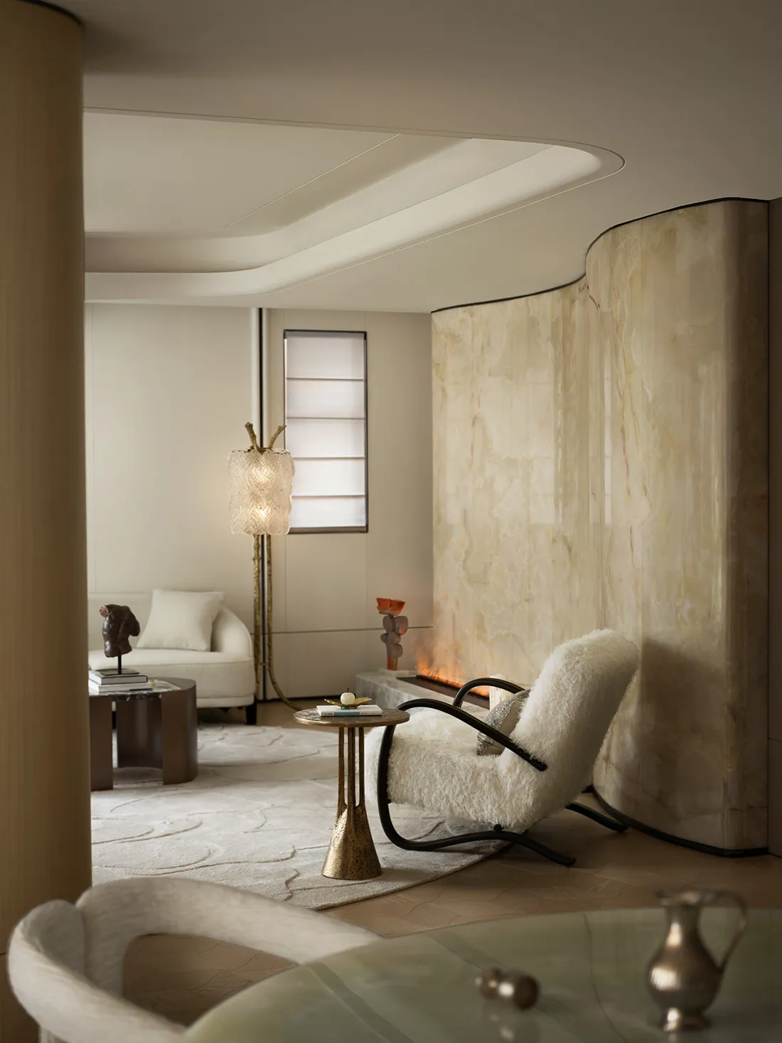 A modern living room with white marble walls and floor, featuring a circular white sofa with colorful cushions and large wind