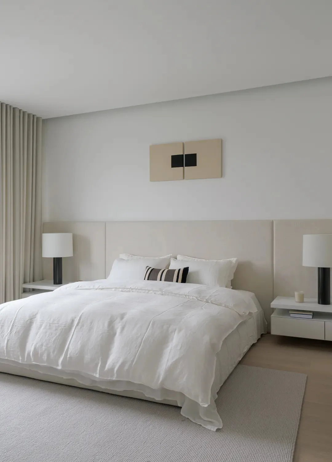 A modern minimalist bedroom with neutral tones, featuring a large bed with white bedding, two side tables with black lamps, a