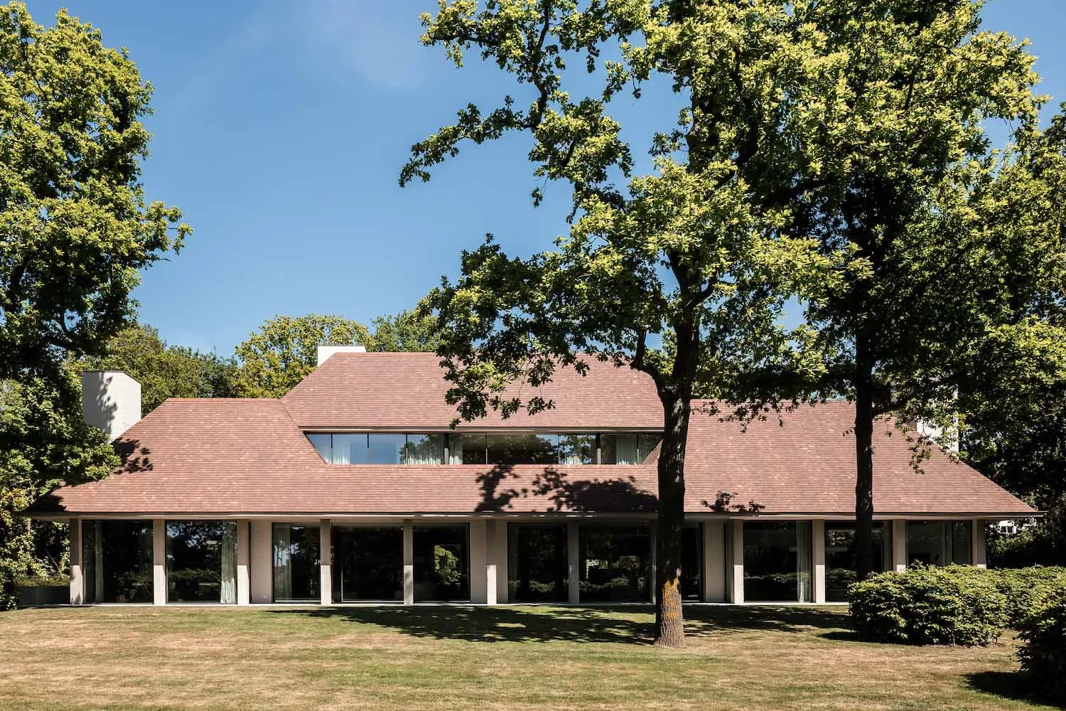 Modern residential building with clay-tiled roof exterior surrounded by green trees and lawn.