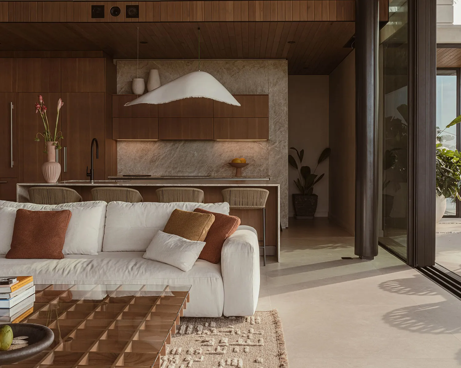 Modern living room with white sofa, wooden floor, marble kitchen counter, and large windows.
