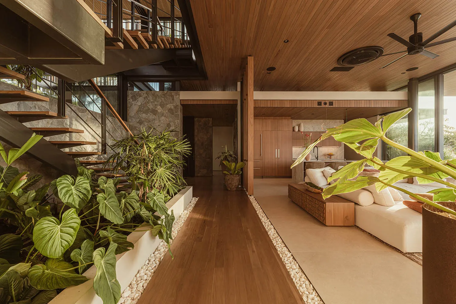 A modern living room with wood elements, including a sofa, plants, and a staircase.