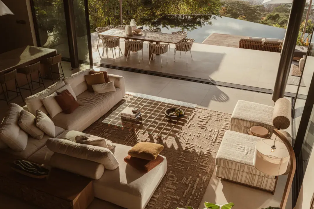 A spacious, modern living room featuring a white sectional sofa with brown and white cushions, a patterned rug, an ottoman, a