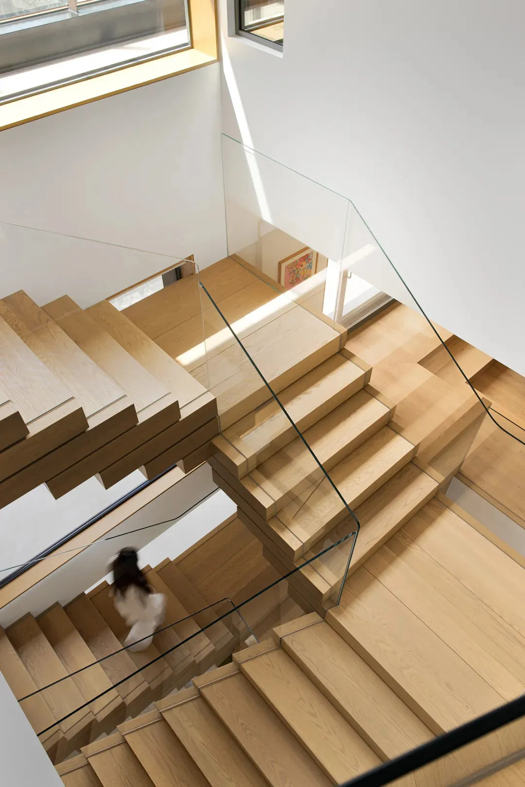 A modern wooden staircase with glass balustrades, viewed from above.