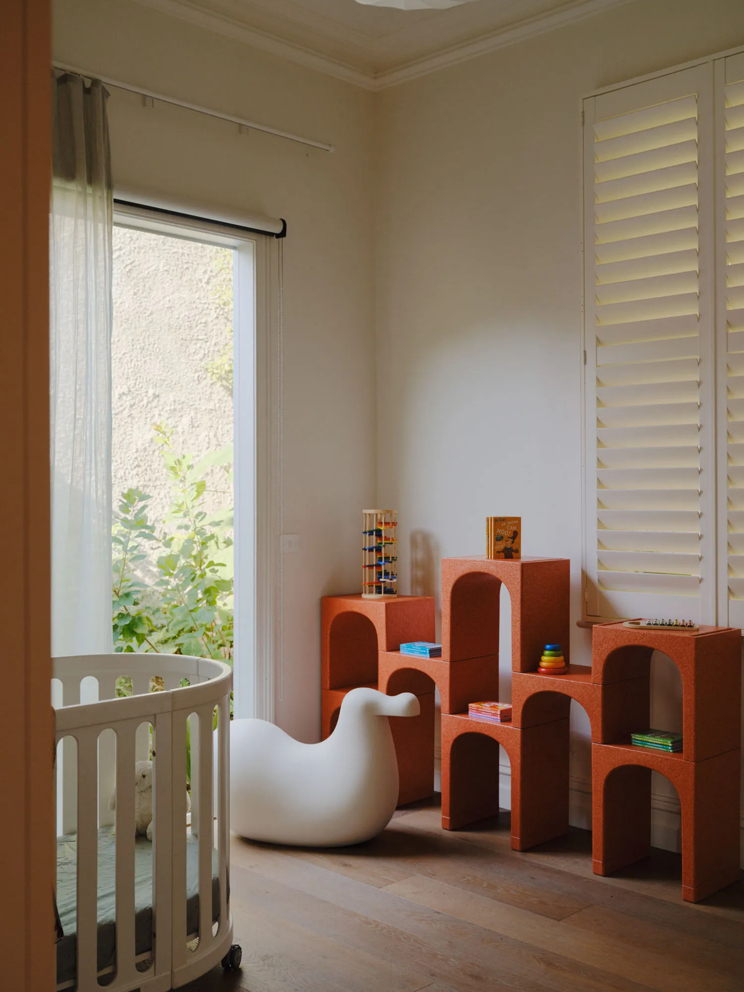 A modern children's bedroom featuring white furniture with bird-shaped armé and orange modular shelving units with children's