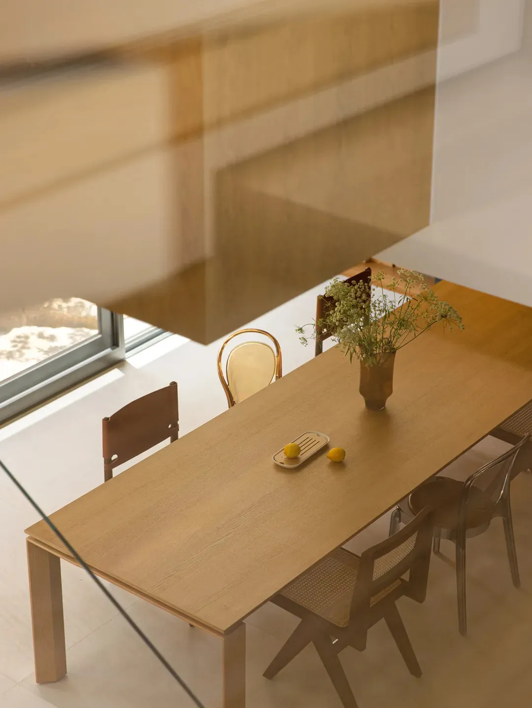 A modern dining room featuring a wooden table with chairs, a vase with flowers, and lemons on a tray.