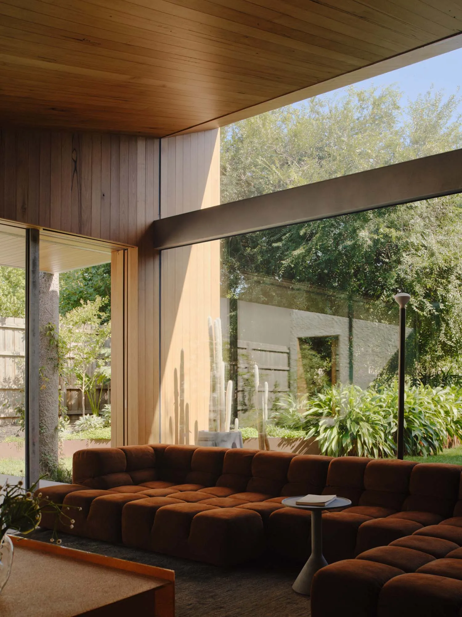 Modern living room featuring a comfortable couch, large glass window, and surrounding greenery.