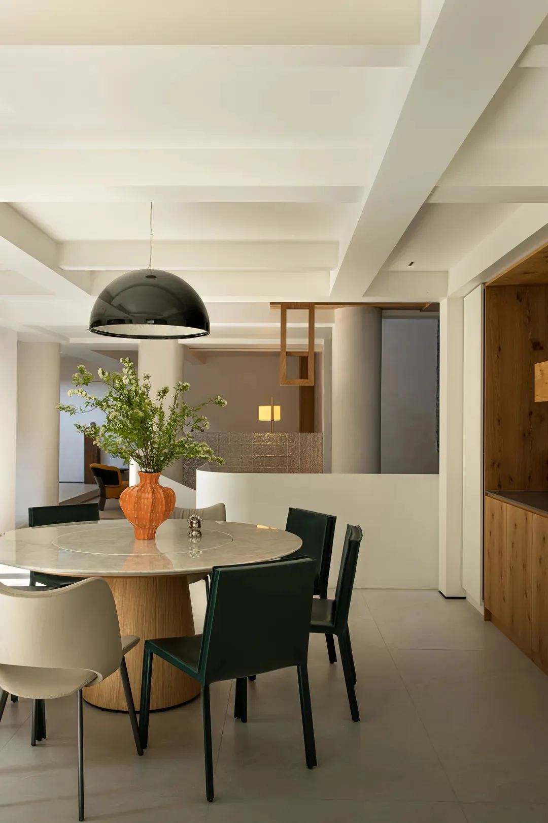 Modern dining room featuring marble table and chairs, wood accents, and a hanging black dome light fixture.
