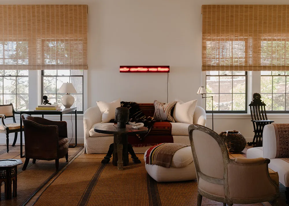 A cozy living room with wooden furniture, including a white sofa, armchairs, and a coffee table, positioned near large window