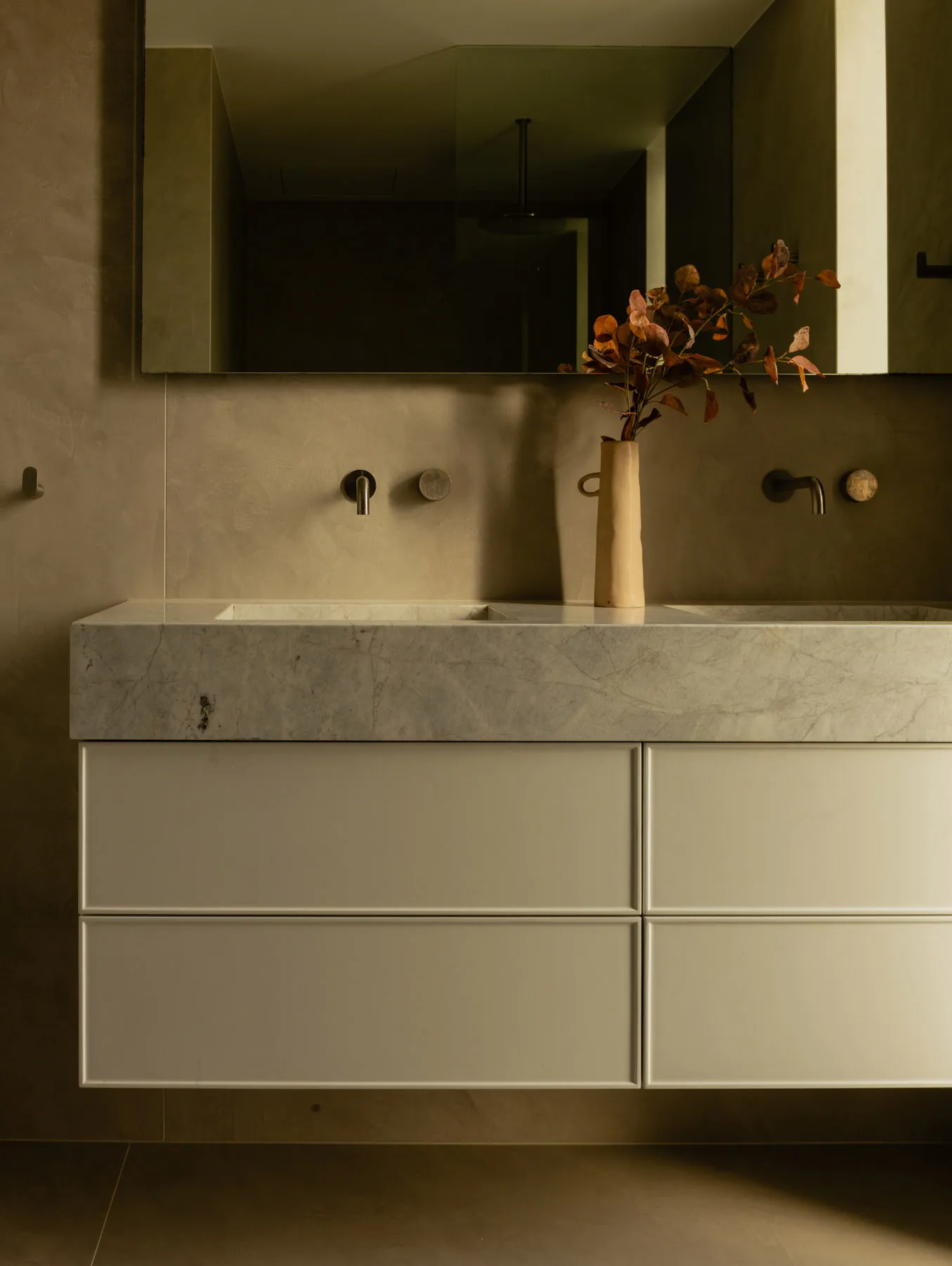 Modern bathroom featuring a marble countertop with a vase of dried leaves.