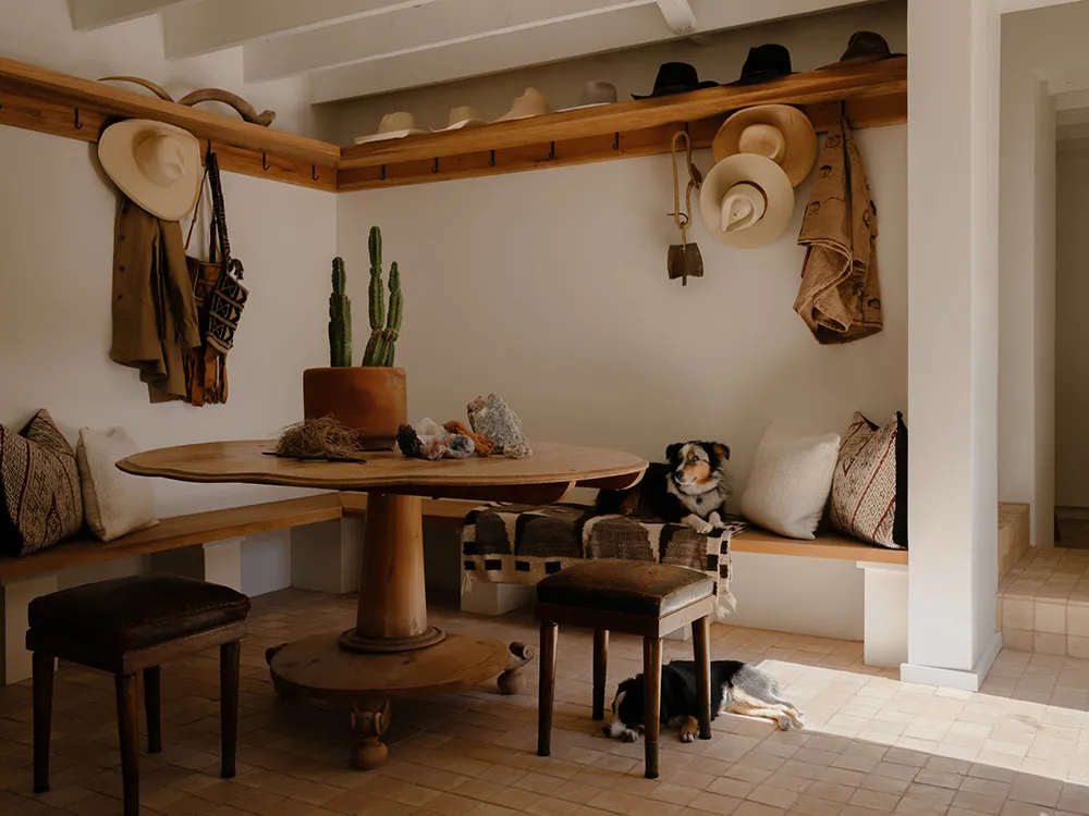 A rustic living room with wooden furniture, a round table, cushions, a cactus plant, and a dog.