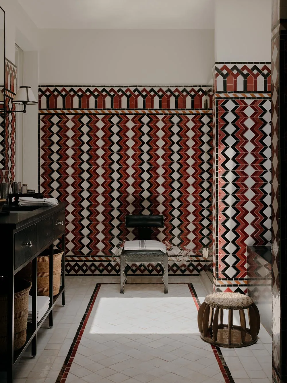 A Victorian-style bathroom with decorative ceramic tiles, a black vanity, and minimalist seating.