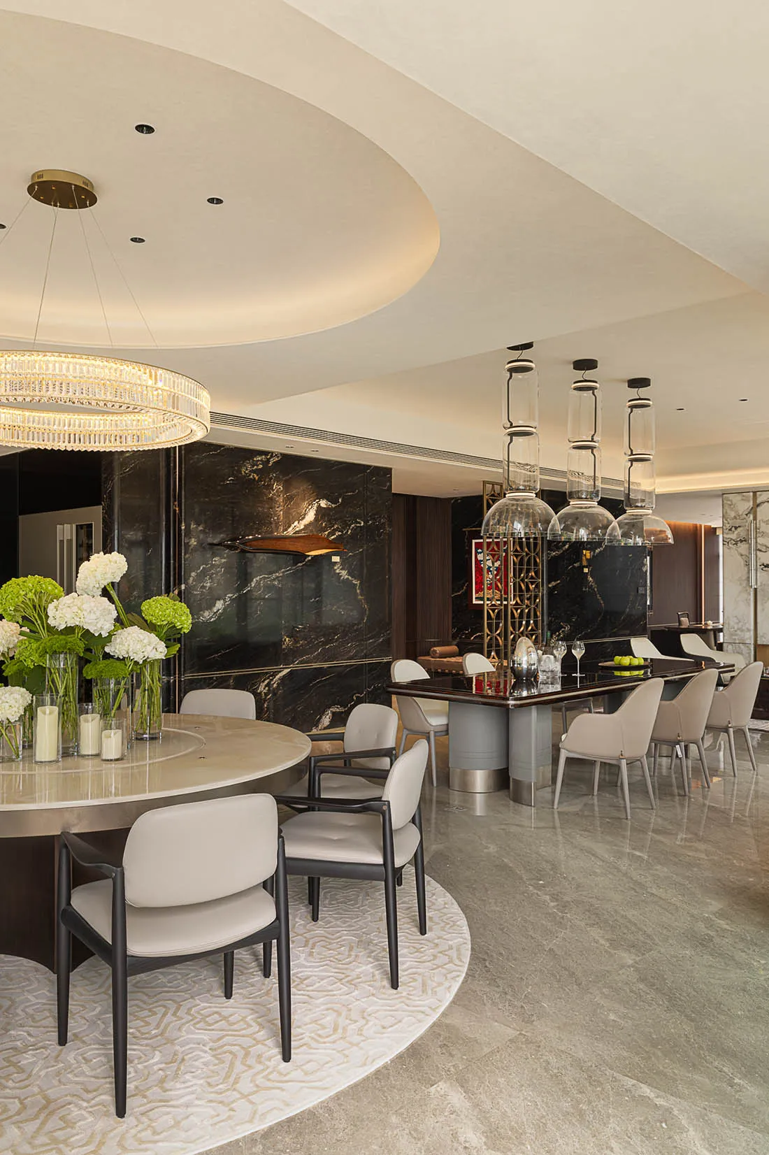 Modern dining room featuring a round marble table and chairs, alongside a bar area with pendant lights and wine storage.