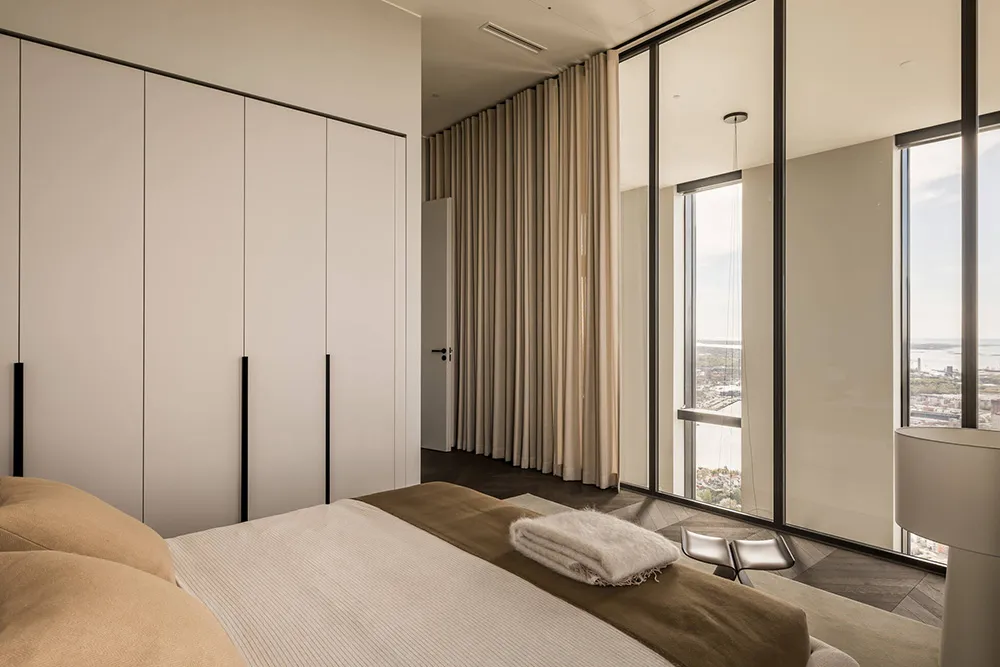 Contemporary bedroom with neutral tones and large windows overlooking a scenic view.