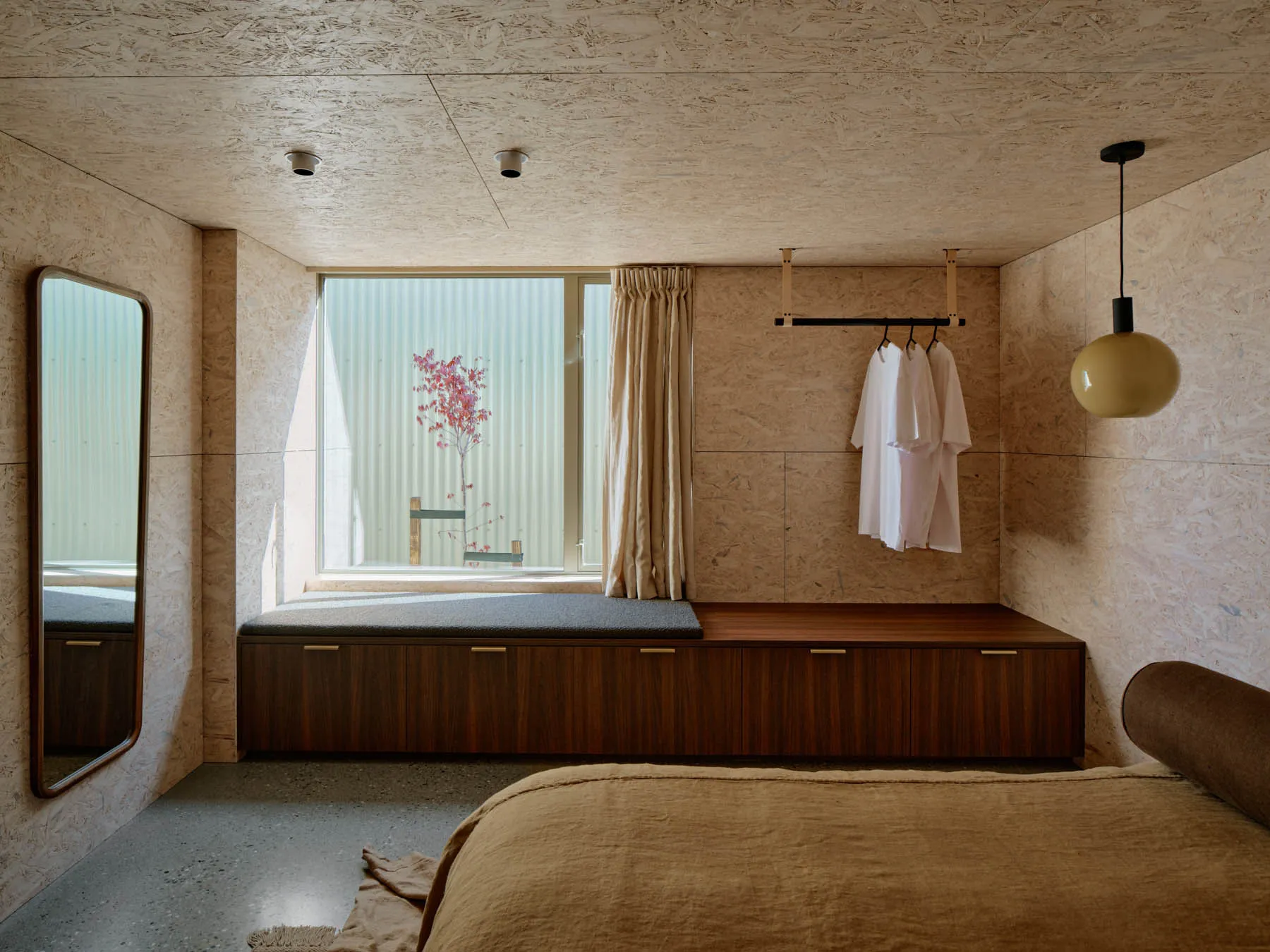 Minimalist bedroom with concrete floor, wooden bench, and hanging garments