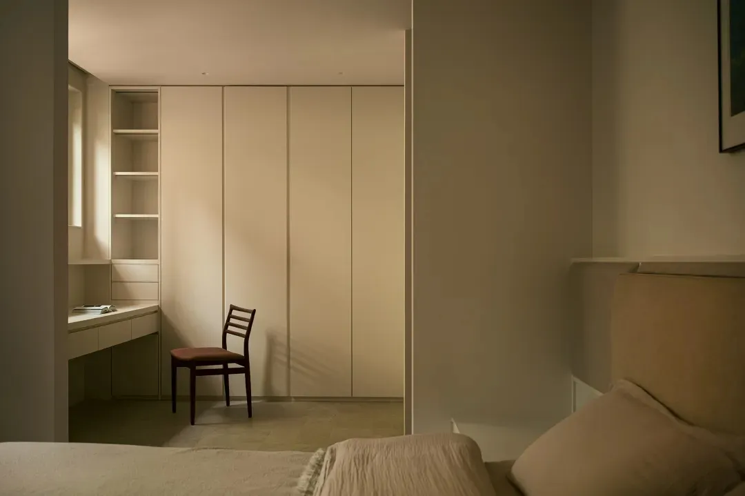 A minimalist bedroom featuring a bed with a neutral-toned upholstered headboard and a beige space-saving wardrobe with a buil