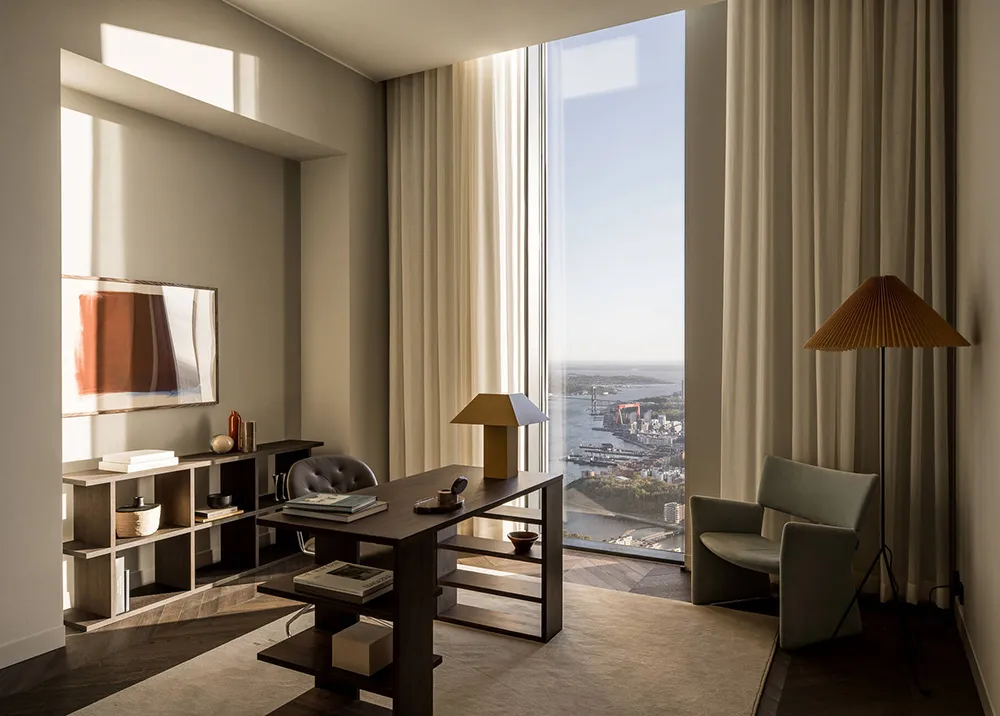 A minimalist office with wooden furniture and marble flooring, featuring a large window with a city view.