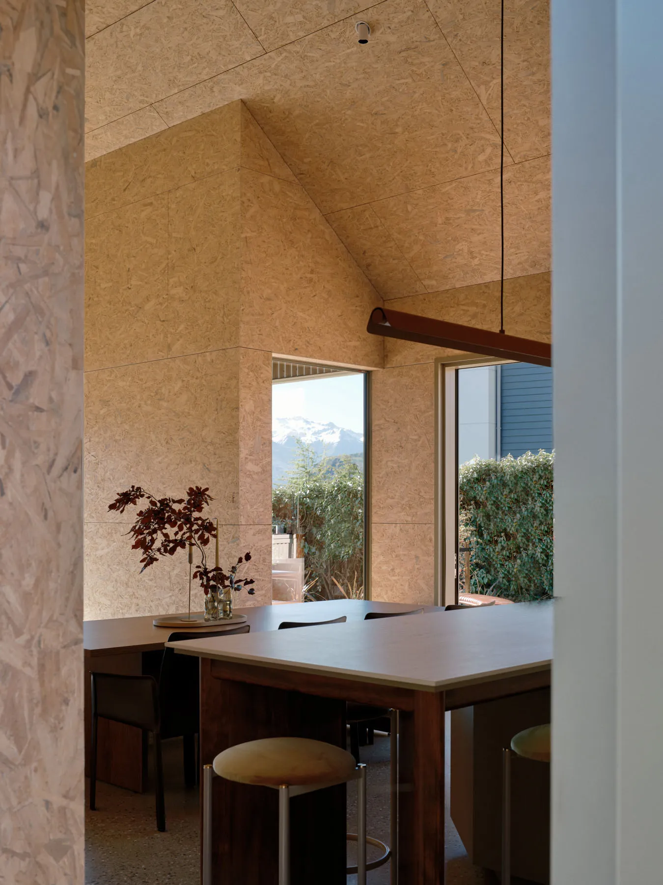A modern dining room featuring wood-oriented strand board walls and a high ceiling with a hanging lamp.