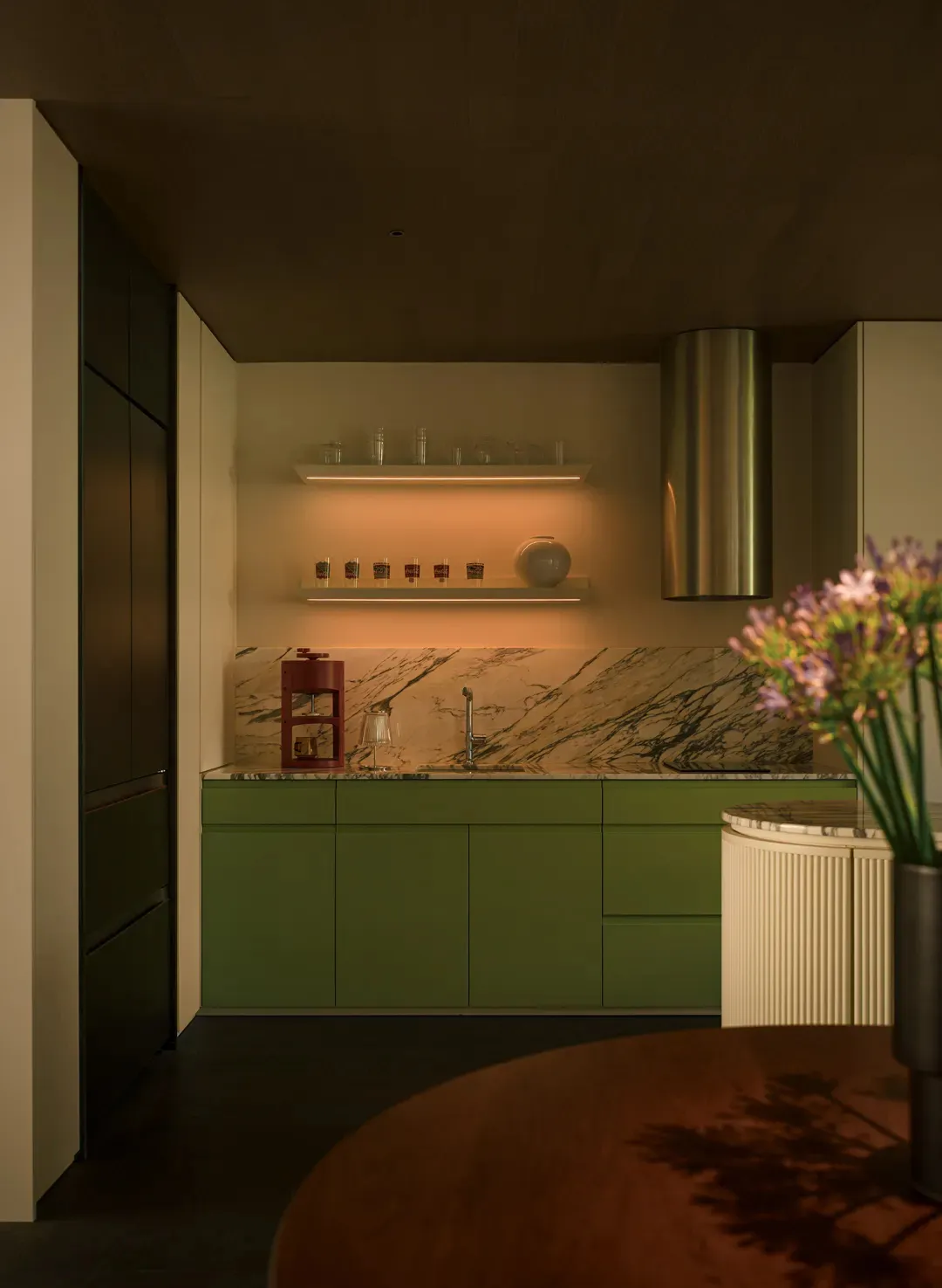 A modern kitchen with green cabinets and a marble backsplash.