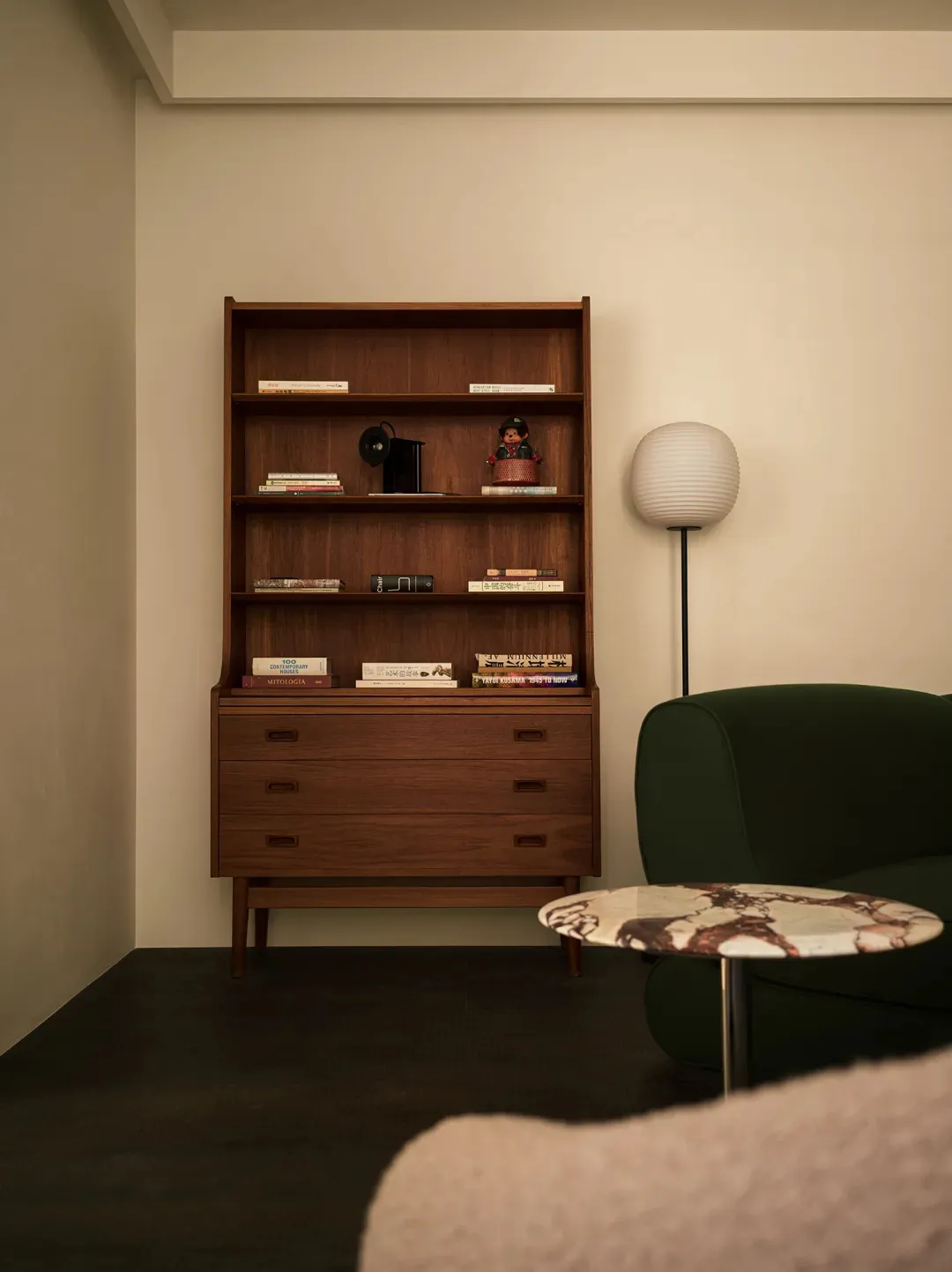 Modern living room with a wooden bookshelf, marble side table, and green armchair.