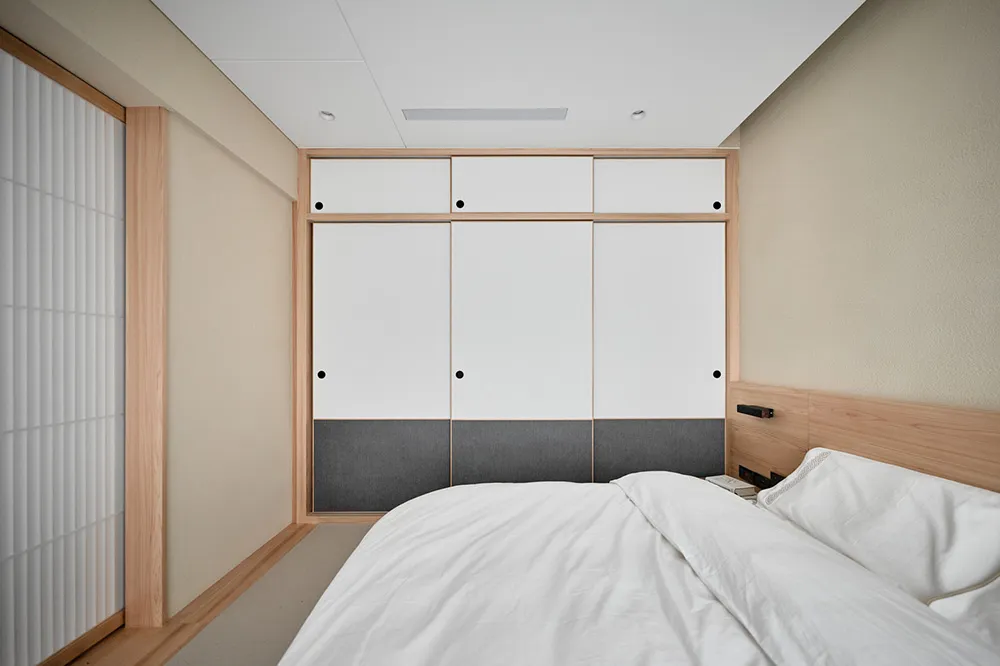 Minimalist bedroom with white walls, wooden floor, and a bed with white bedding.