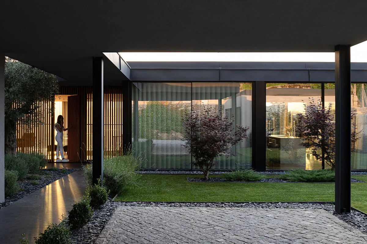A modern minimalist house featuring glass, concrete, and a neatly maintained lawn.